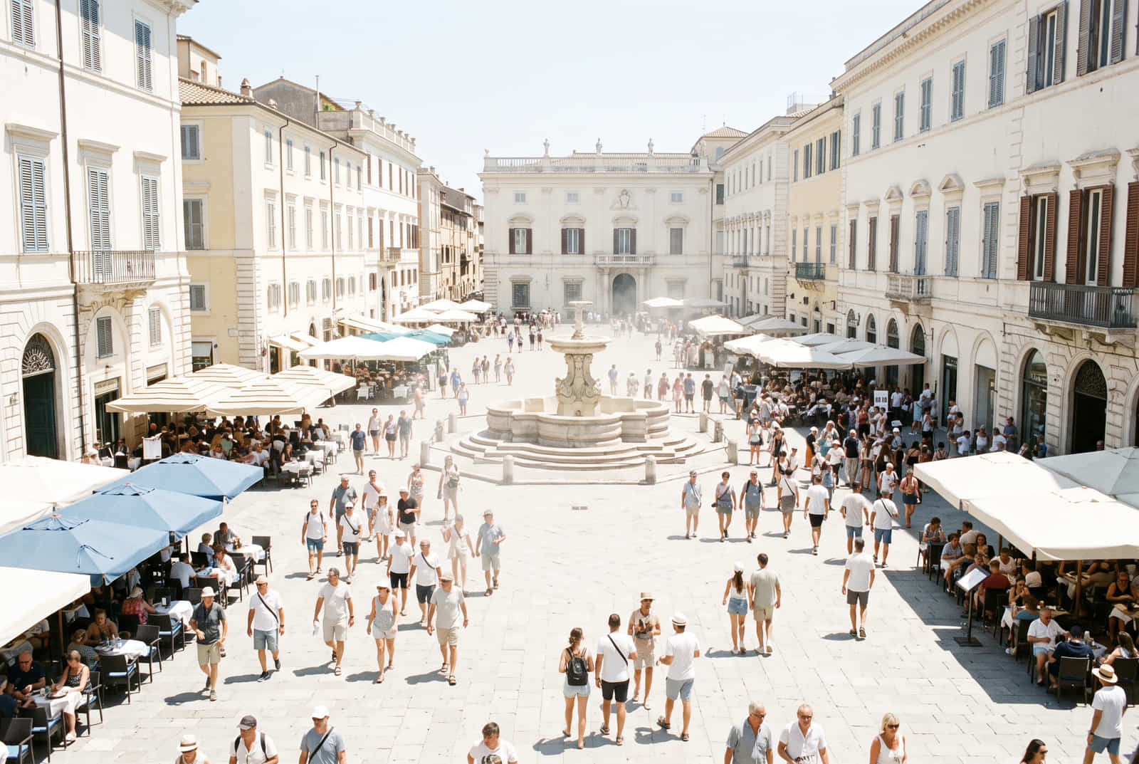 A crowded European city square at midday in high summer, packed with people under harsh bleaching sunlight